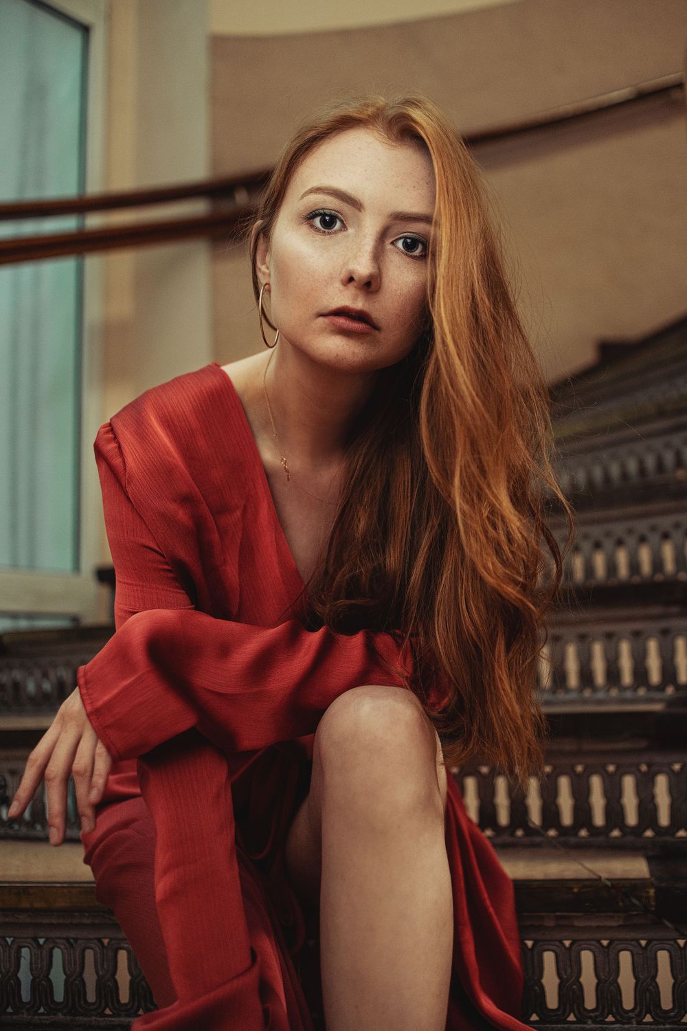 Dramatic portrait on ornate staircase in red evening dress.