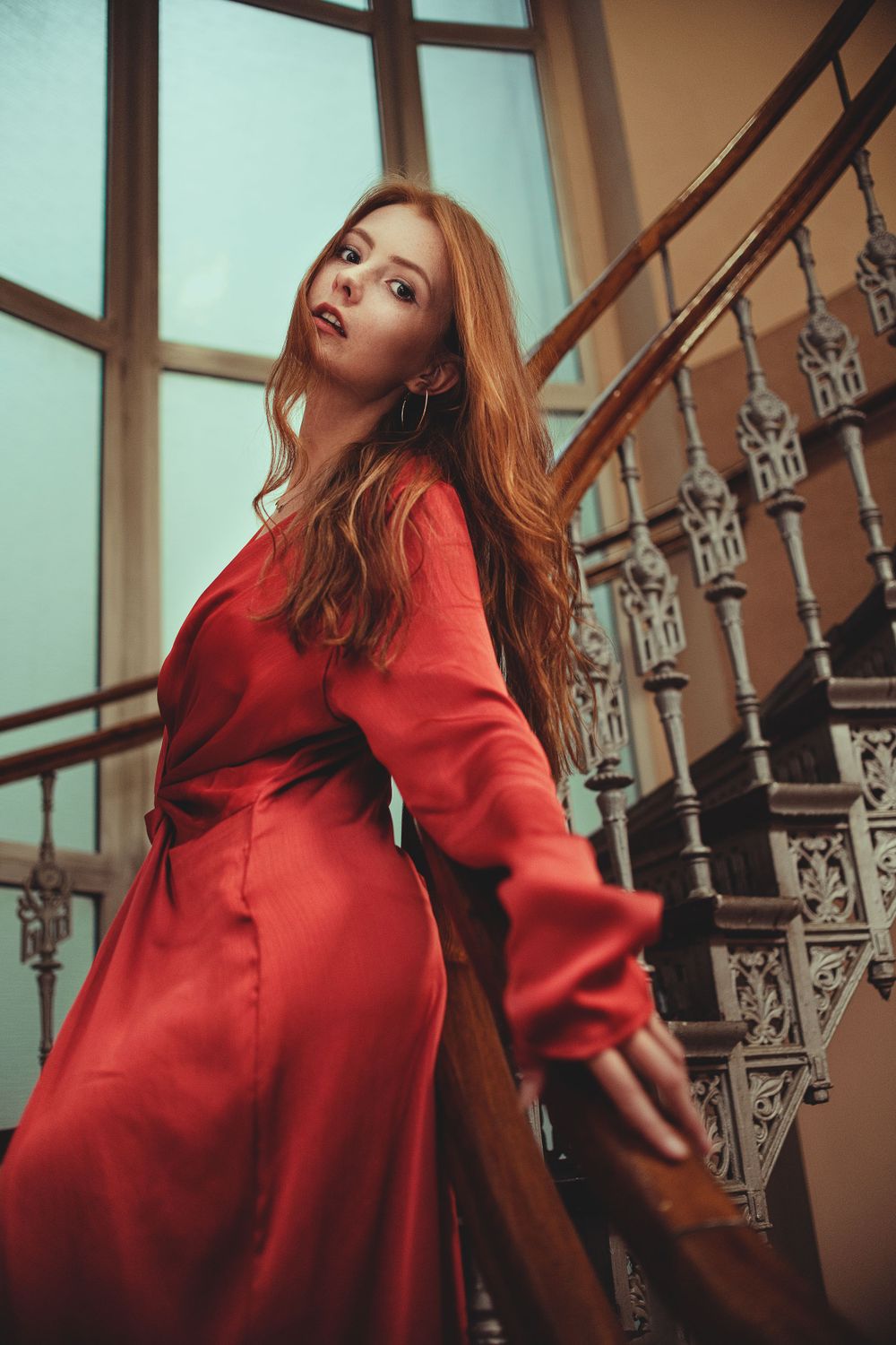 Artistic sequence in red outfit against vintage staircase with decorative metalwork.