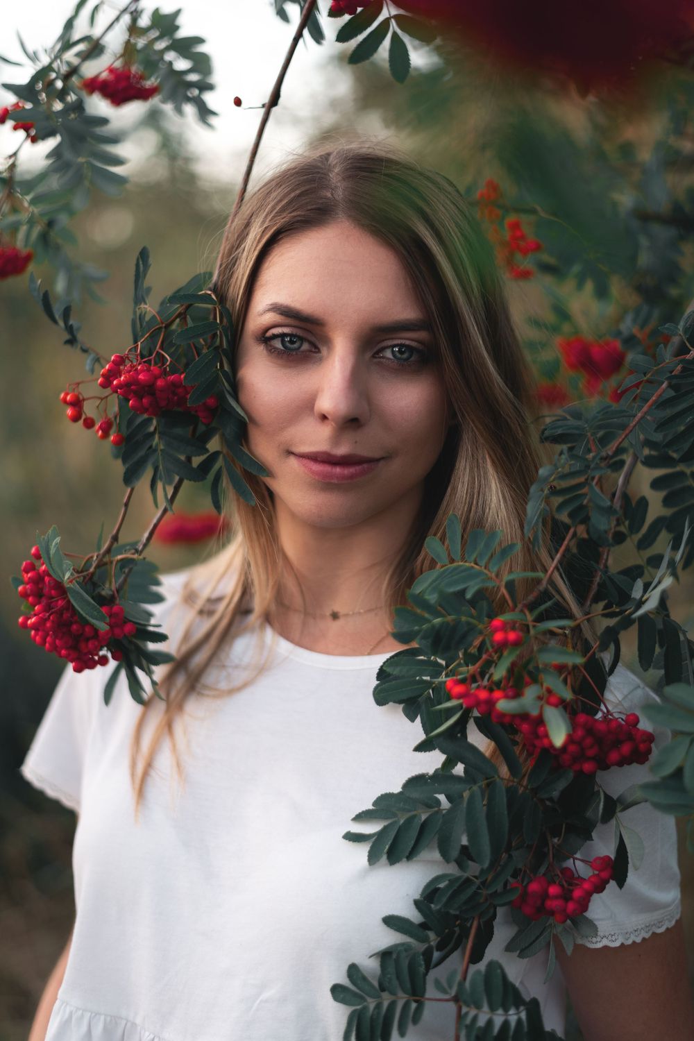 Portrait framed by red berries and green foliage wearing white t-shirt.