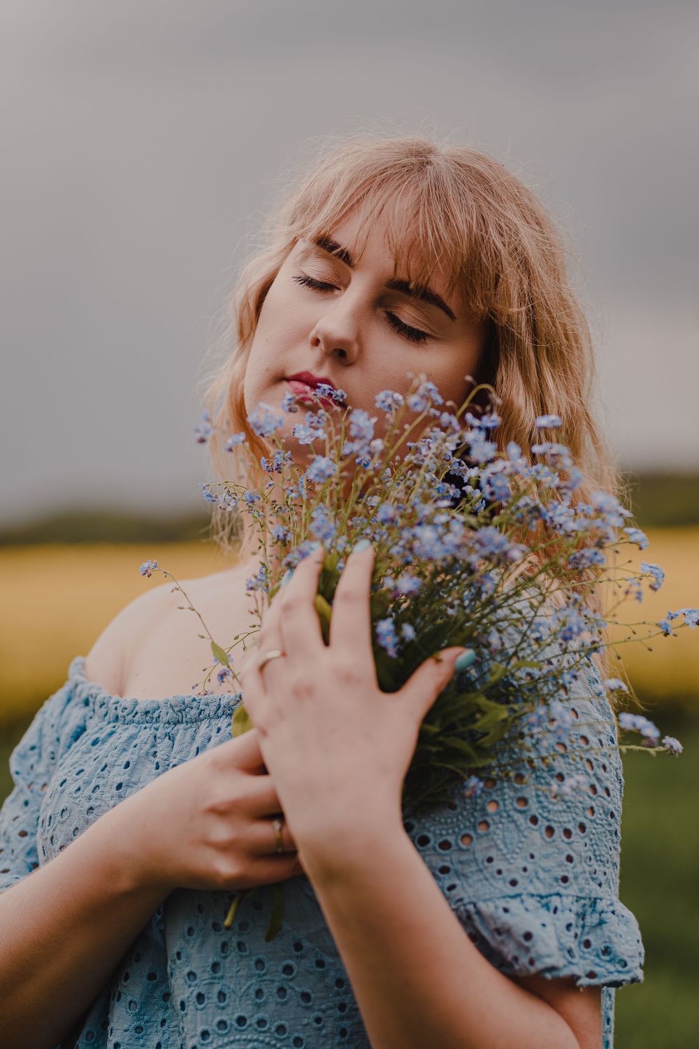 Person in blue dress joyfully embracing wildflowers in a summer field.