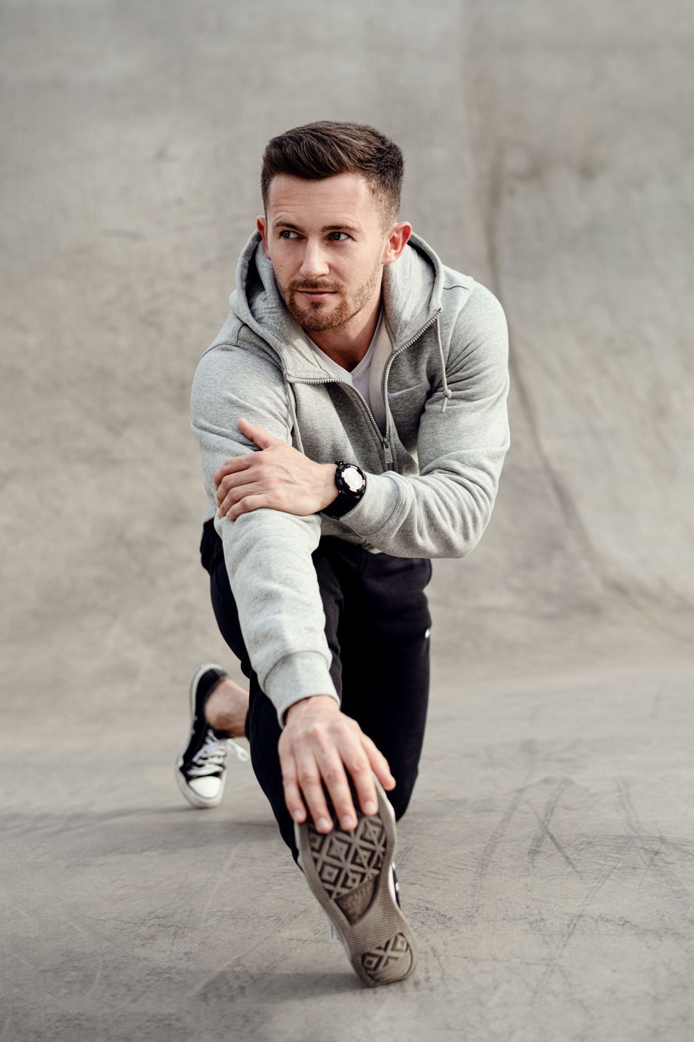 Athletic figure in grey hoodie demonstrating various crouching poses against concrete background.