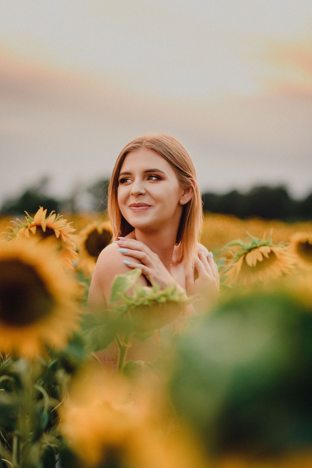 Artistic portrait among blooming sunflowers at sunset.