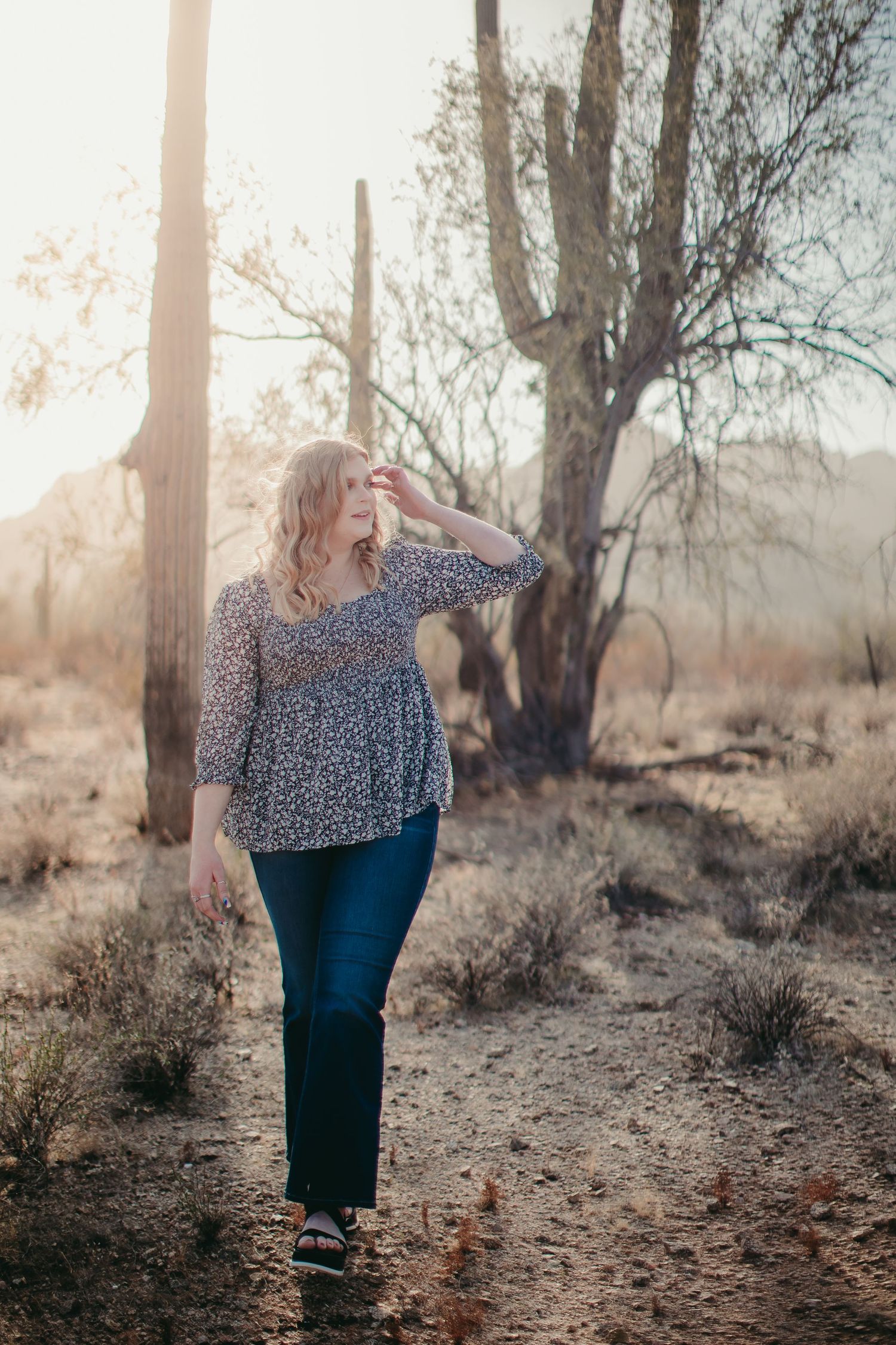 A floral print top and jeans outfit photographed in a desert landscape with saguaro cacti at golden hour.