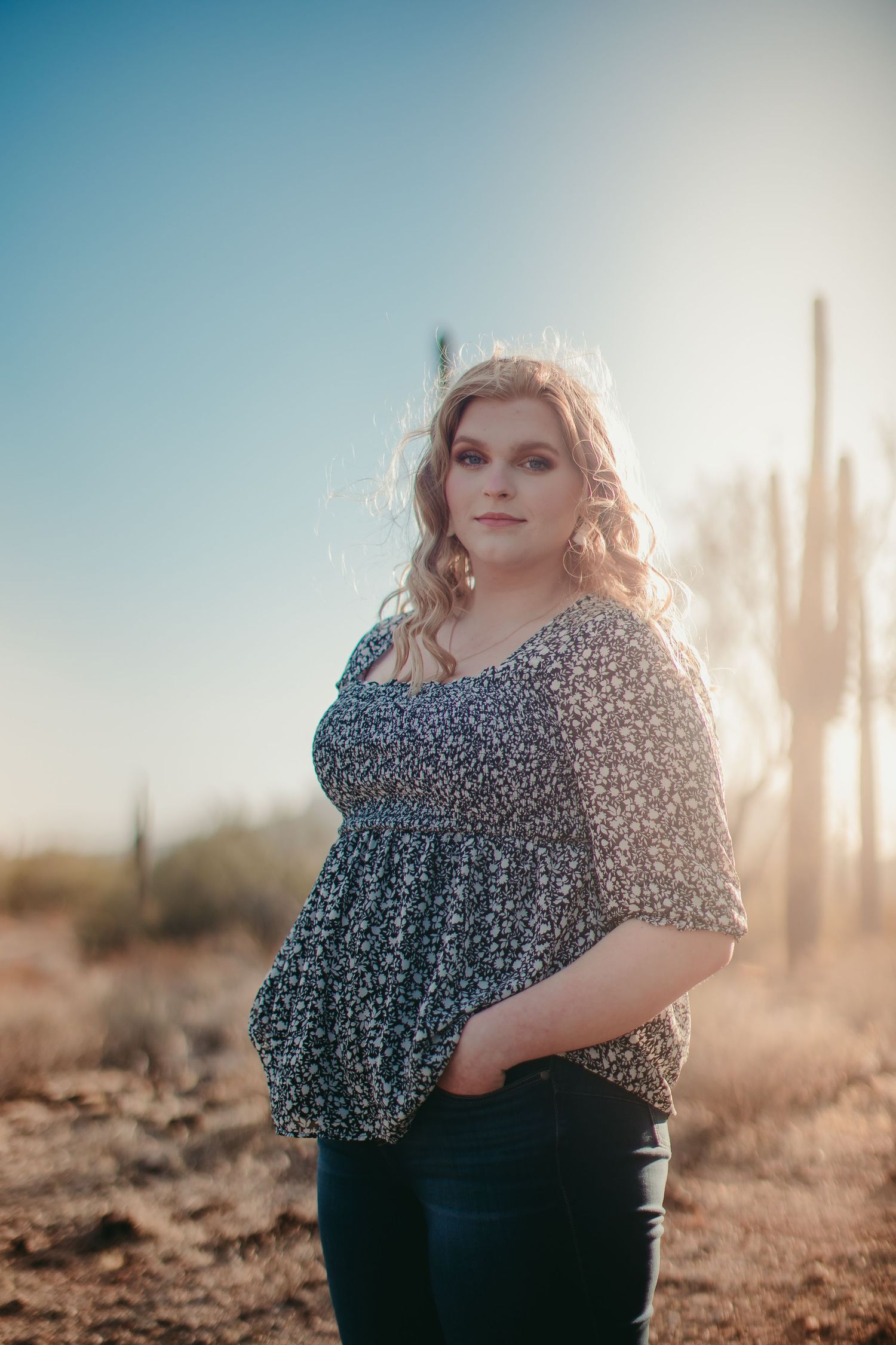 Fashion portrait in a desert setting with saguaro cacti and blue sky background.
