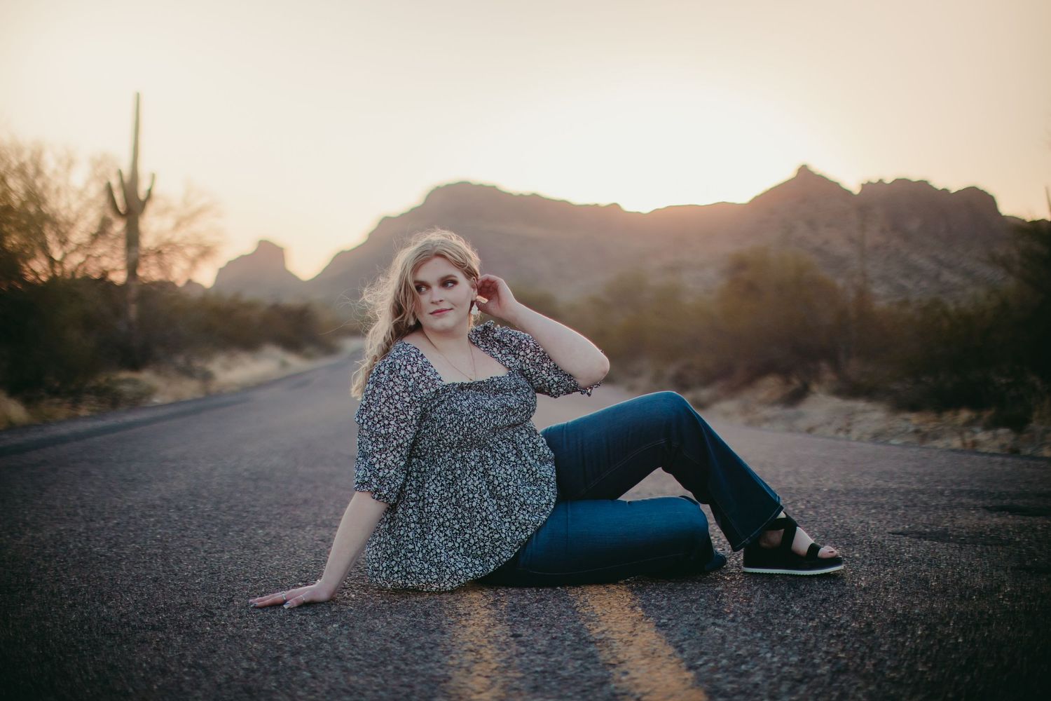 Casual outdoor portrait session on a desert road with mountains in the background at sunset.
