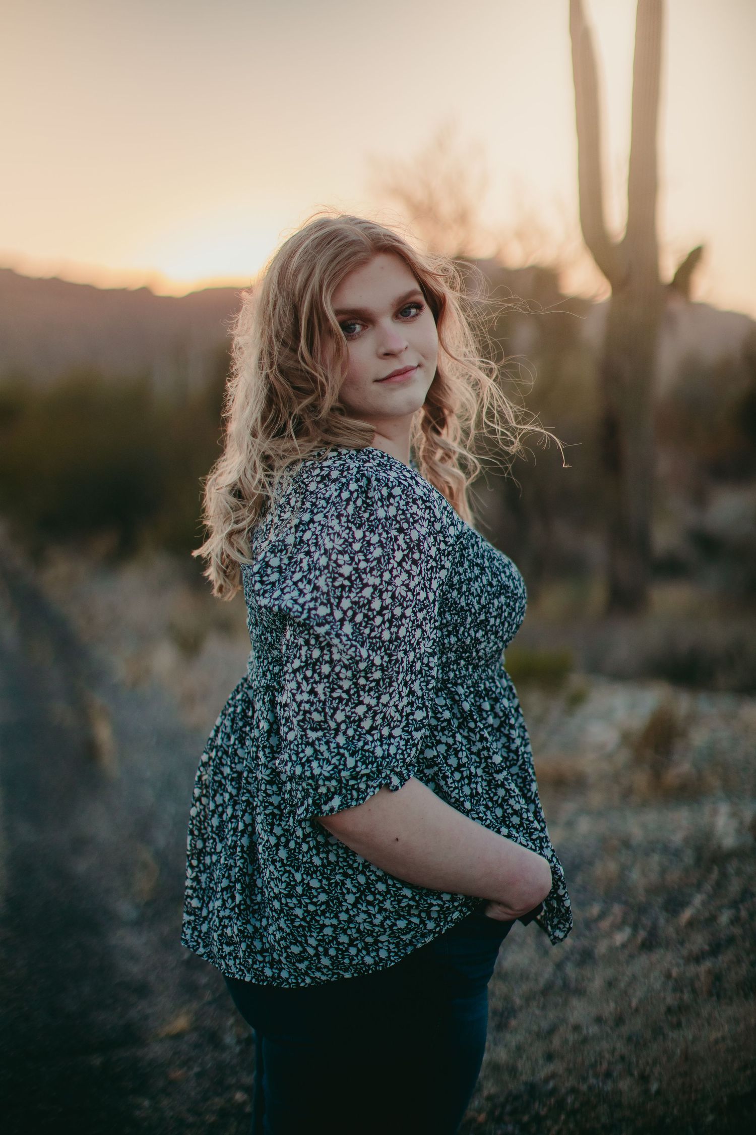 Artistic desert photoshoot featuring a floral print top against a sunset mountain backdrop.