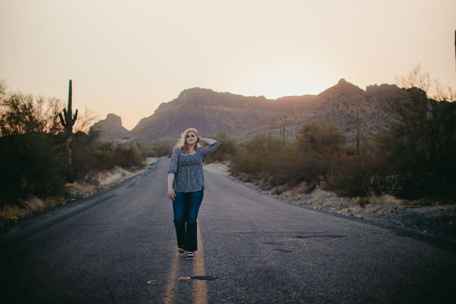 Lifestyle portrait on an empty desert road with mountain silhouettes at dusk.
