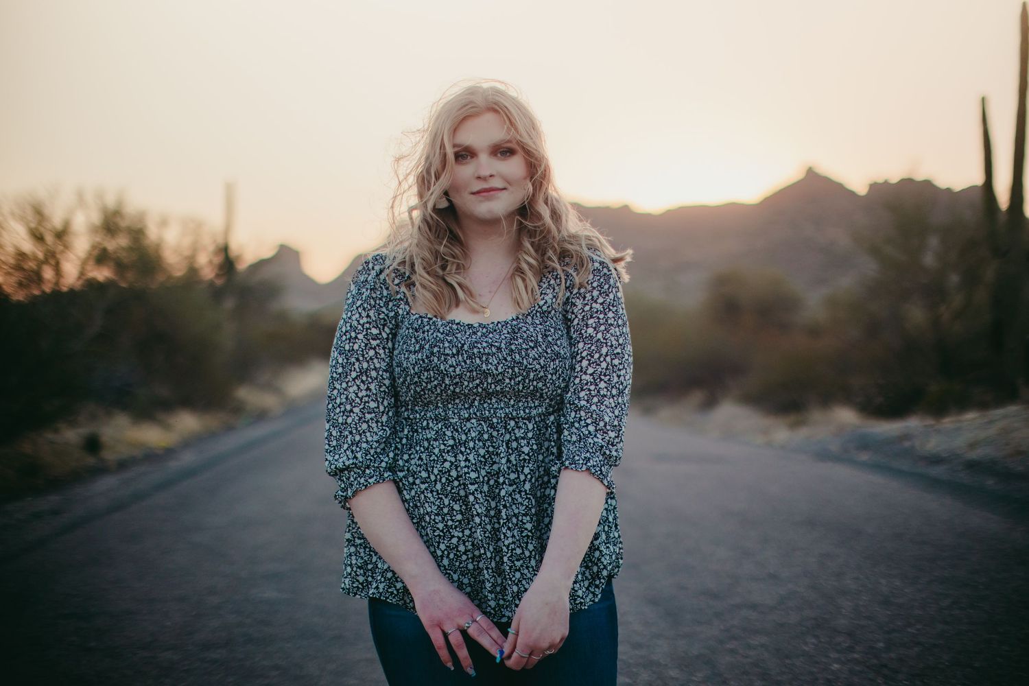 Sunset portrait session on a desert road with mountains and saguaro cacti in the background.