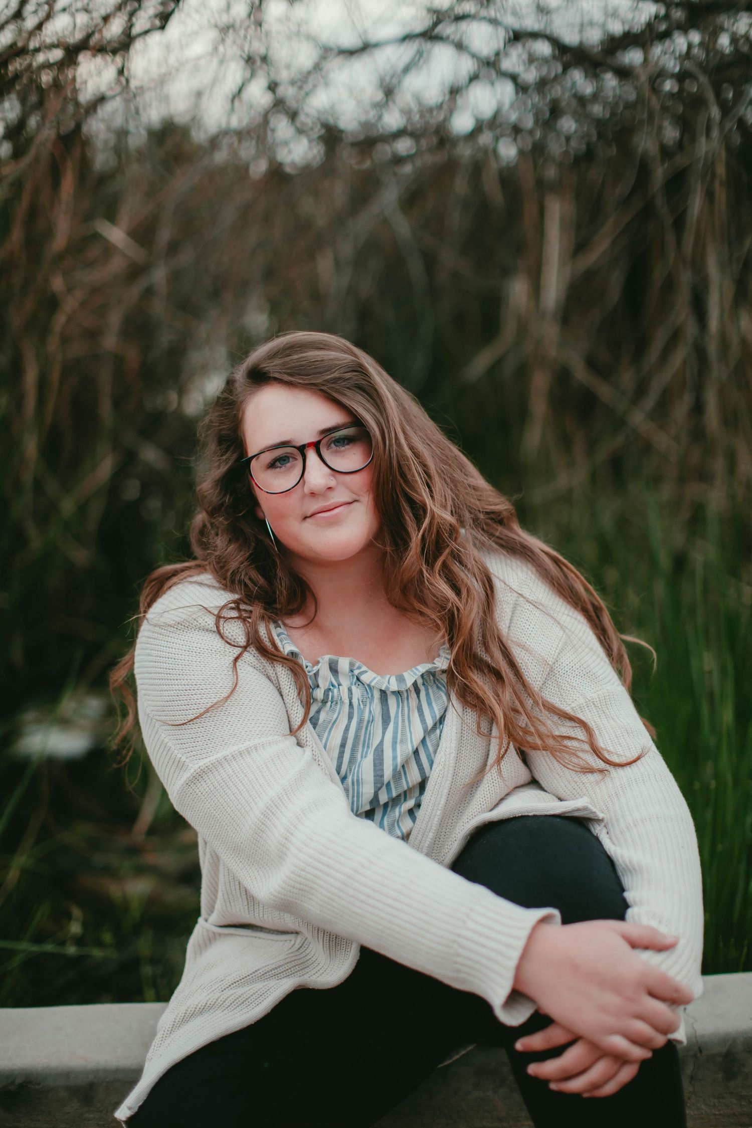 Person in cozy cream sweater sits casually outdoors during portrait session.