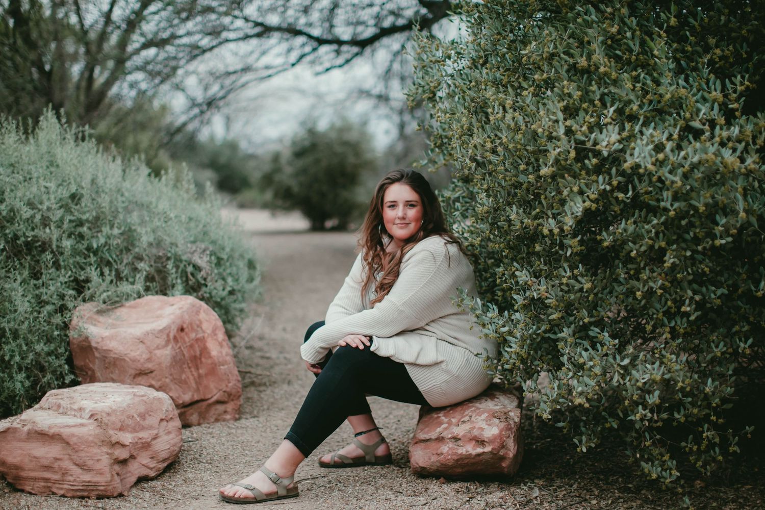 Casual outdoor portrait sitting on pink rocks surrounded by desert vegetation.
