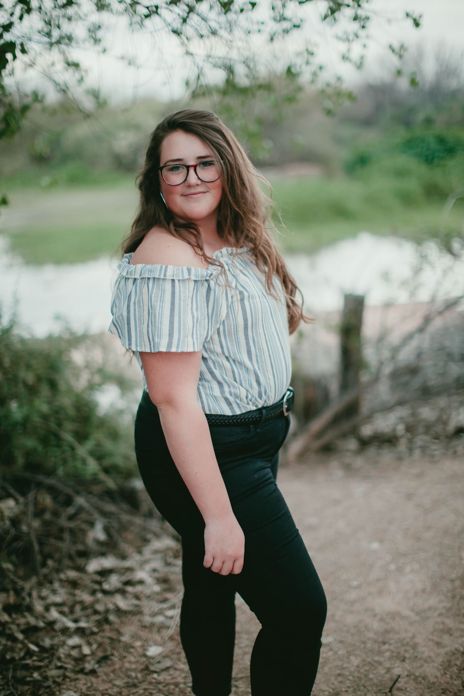 Stylish off-shoulder striped top and dark pants outfit on a nature trail.