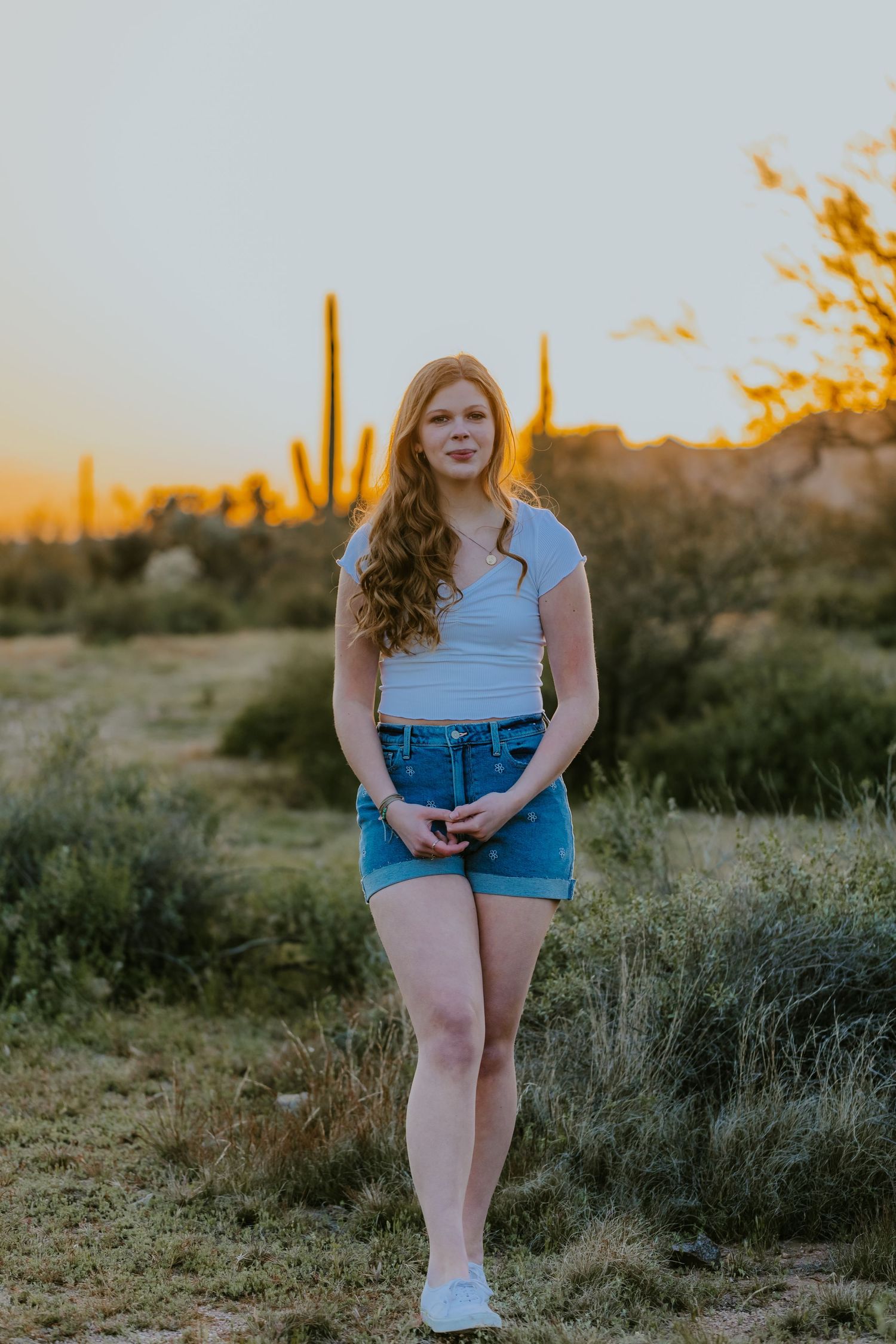 A casual outdoor portrait session in a desert landscape at golden hour with denim shorts and white top.