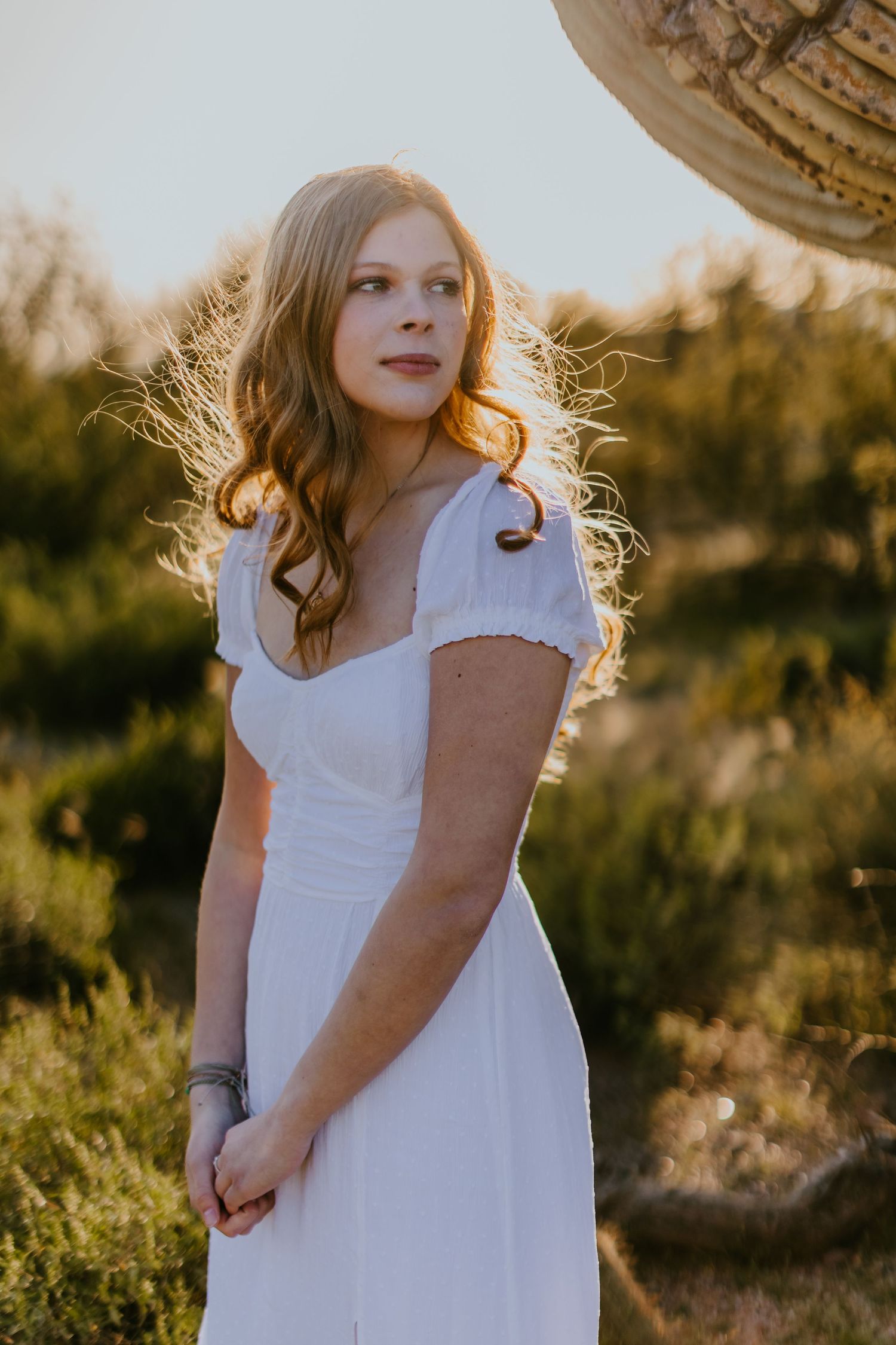 Desert photoshoot featuring a white sundress against natural desert flora during sunset.