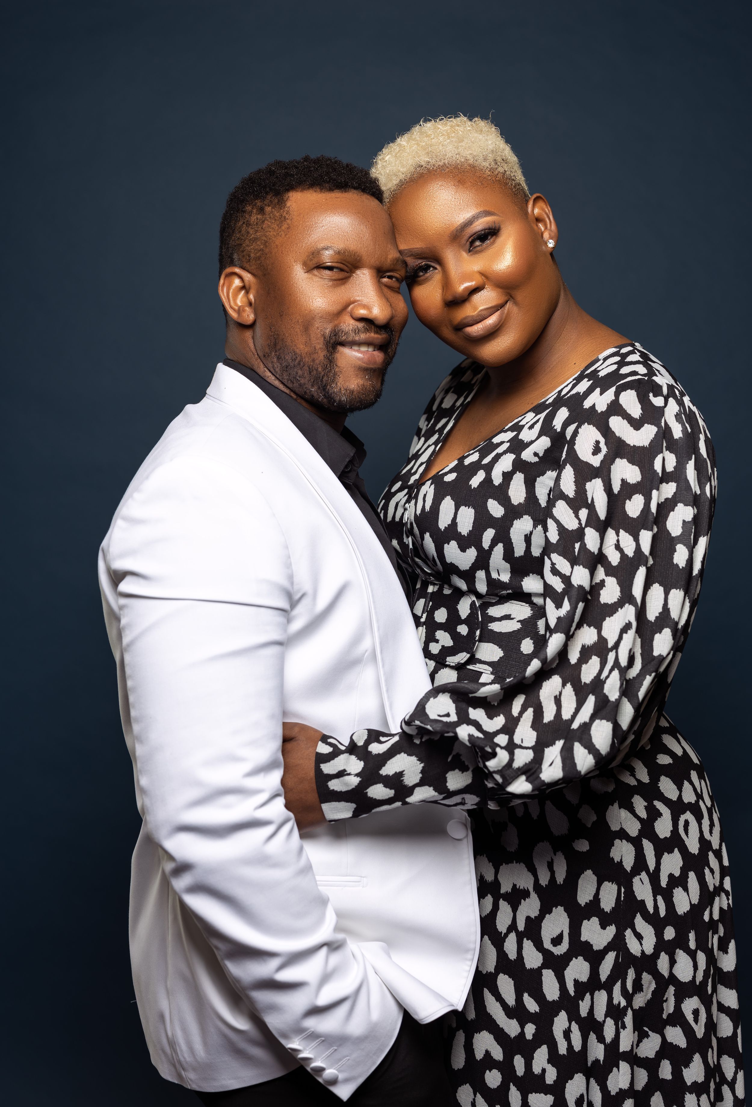 Intimate studio portrait of couple in white blazer and patterned dress showing affection.