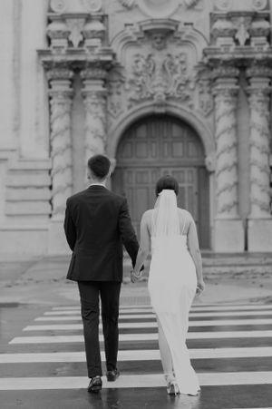 Black and white photo of couple walking towards ornate church doors in wedding attire.