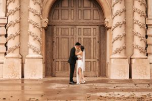 Intimate moment between newlyweds in front of ornate church doors with classical architecture.