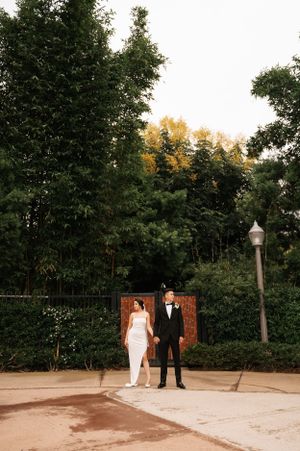 Wedding couple standing against lush garden backdrop with wooden fence.