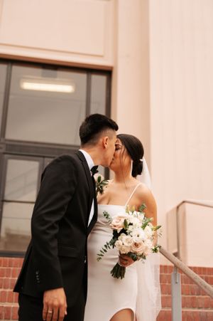 Romantic moment between newlyweds on brick steps with bride holding white floral bouquet.