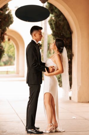 Wedding couple shares playful moment under elegant archways at golden hour.