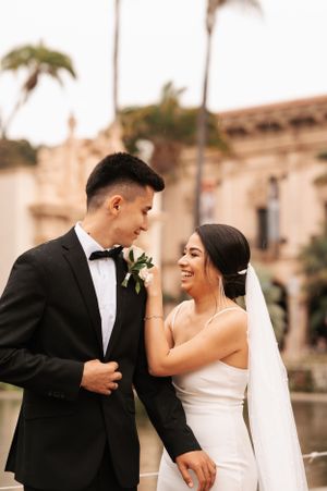 Newlyweds share joyful laughter during their wedding photoshoot near palm trees.