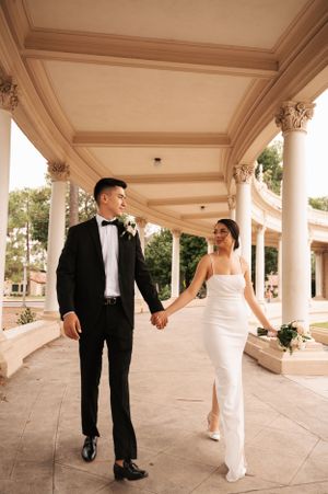 Elegant couple walking under ornate columns in formal wedding attire at a classic venue.
