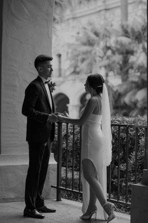 Black and white wedding photo captures intimate moment between bride and groom on balcony.