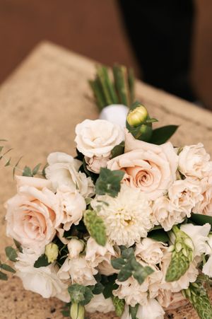 Close-up of romantic wedding bouquet with pale pink roses and white blooms on rustic surface.