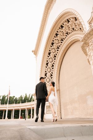 Wedding couple standing beneath ornate archway architecture at sunset.