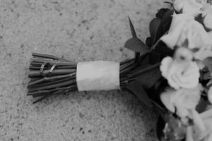 A black and white image of a wedding bouquet with flowers wrapped in white ribbon on a textured surface.