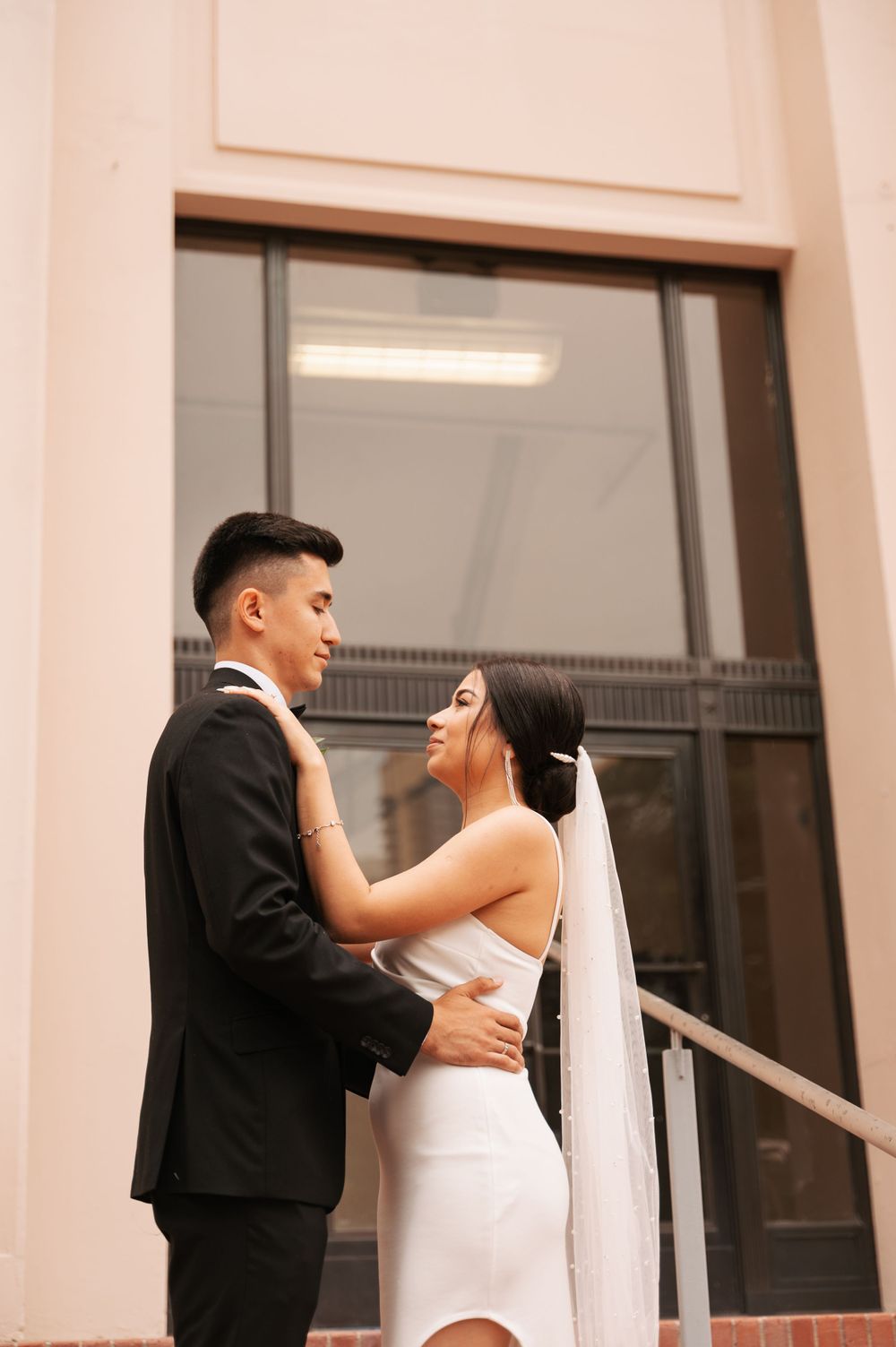 Elegant couple shares intimate moment during wedding photoshoot against neutral wall.