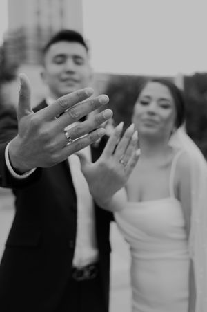Black and white photo showing close up of wedding rings on newlyweds hands.