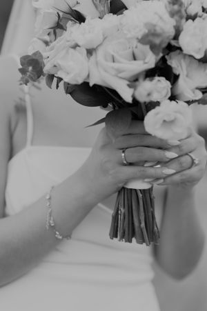 Black and white photo of hands holding wedding bouquet with bracelet and ring details.