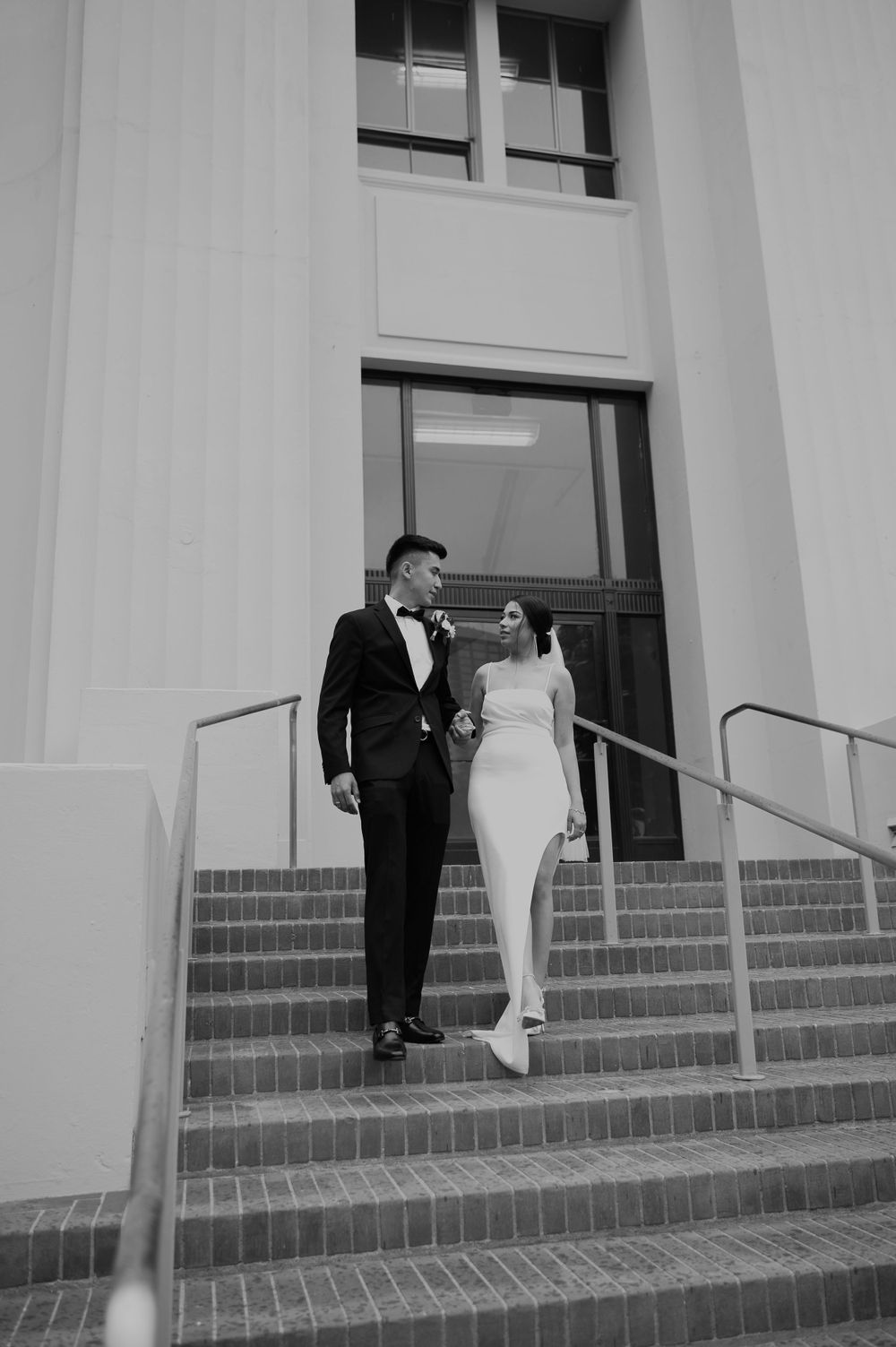 Black and white wedding photo of couple on brick steps with architectural columns.