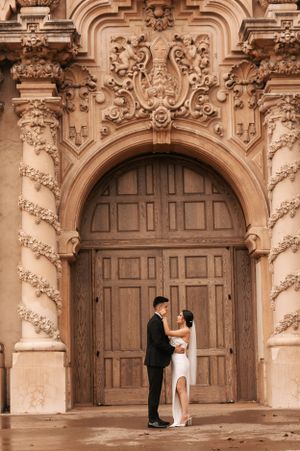 Romantic wedding couple standing in front of grand baroque church doorway with detailed architecture.