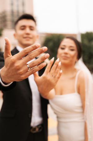 Close up of hands showing wedding rings with couple in soft focus background.