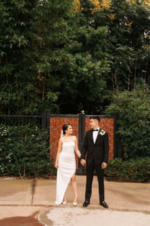 Full-length portrait of newlyweds in front of wooden gate and garden setting.