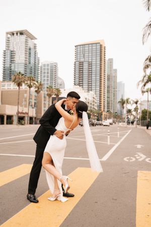 Romantic dip pose of newlyweds on city street with high-rise buildings in background.