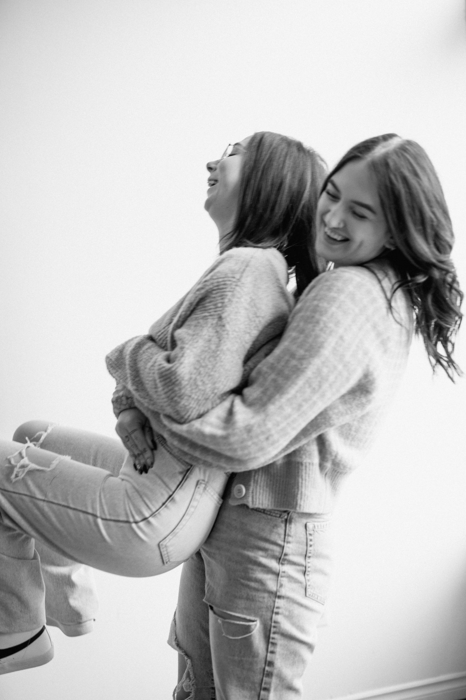 Two friends in sweaters laughing and hugging in a joyful black and white portrait.