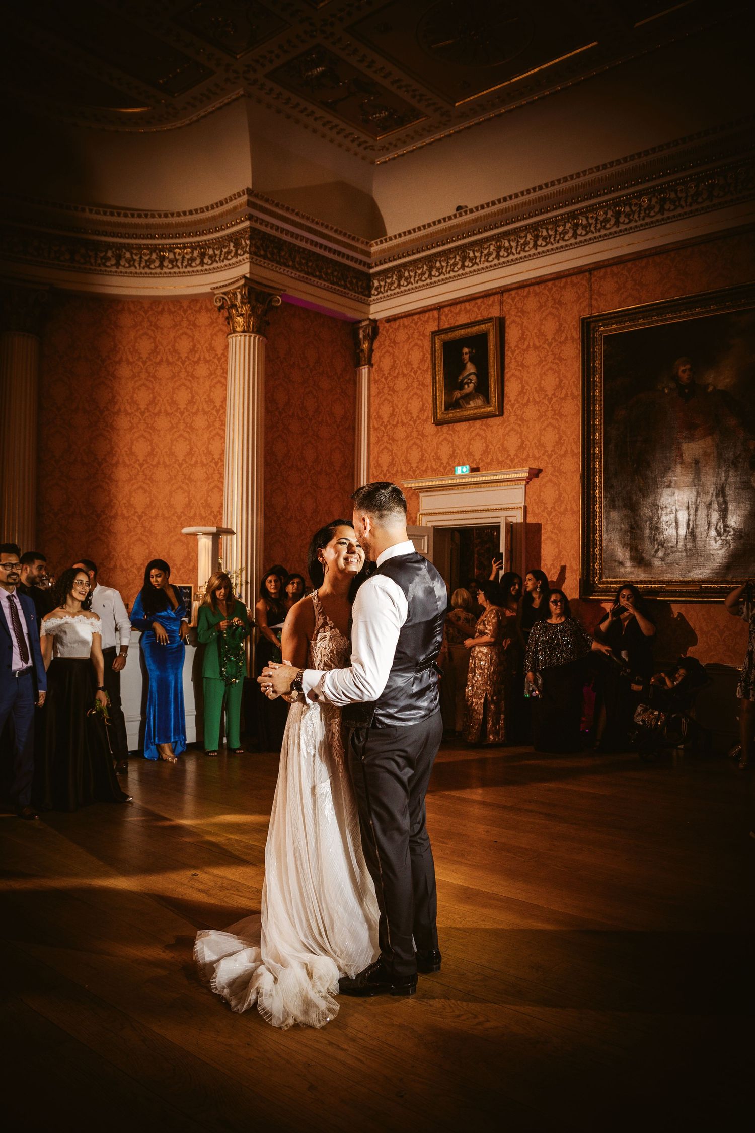A romantic wedding dance moment captured in an ornate ballroom with peach-colored damask walls.