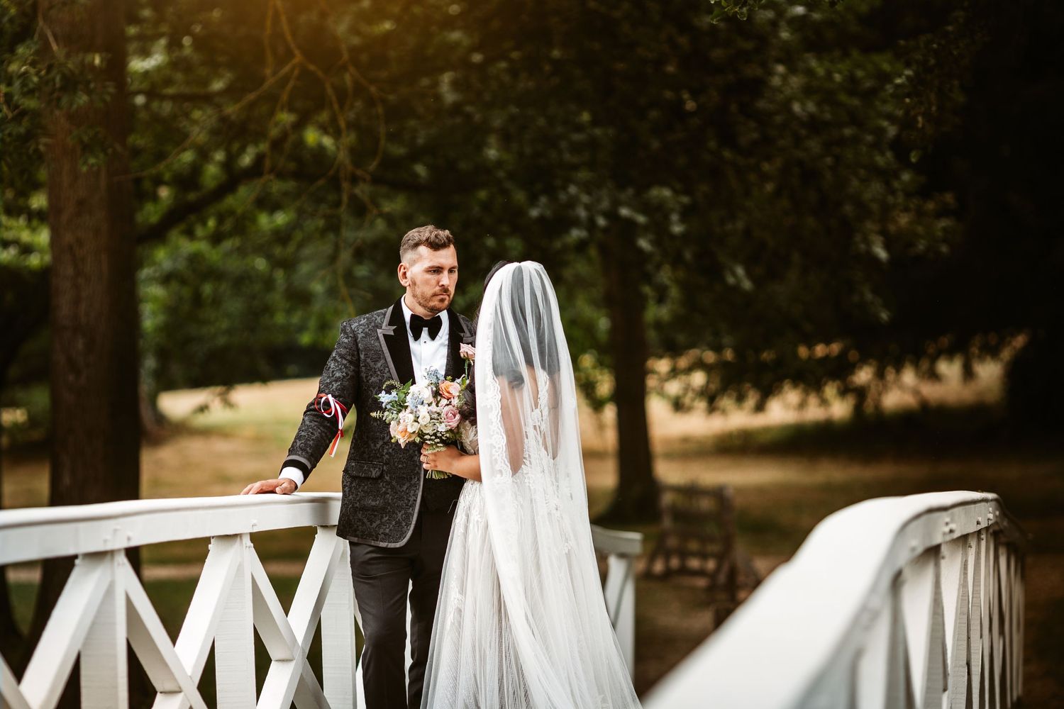 Wedding couple poses on elegant white wooden bridge in park setting.