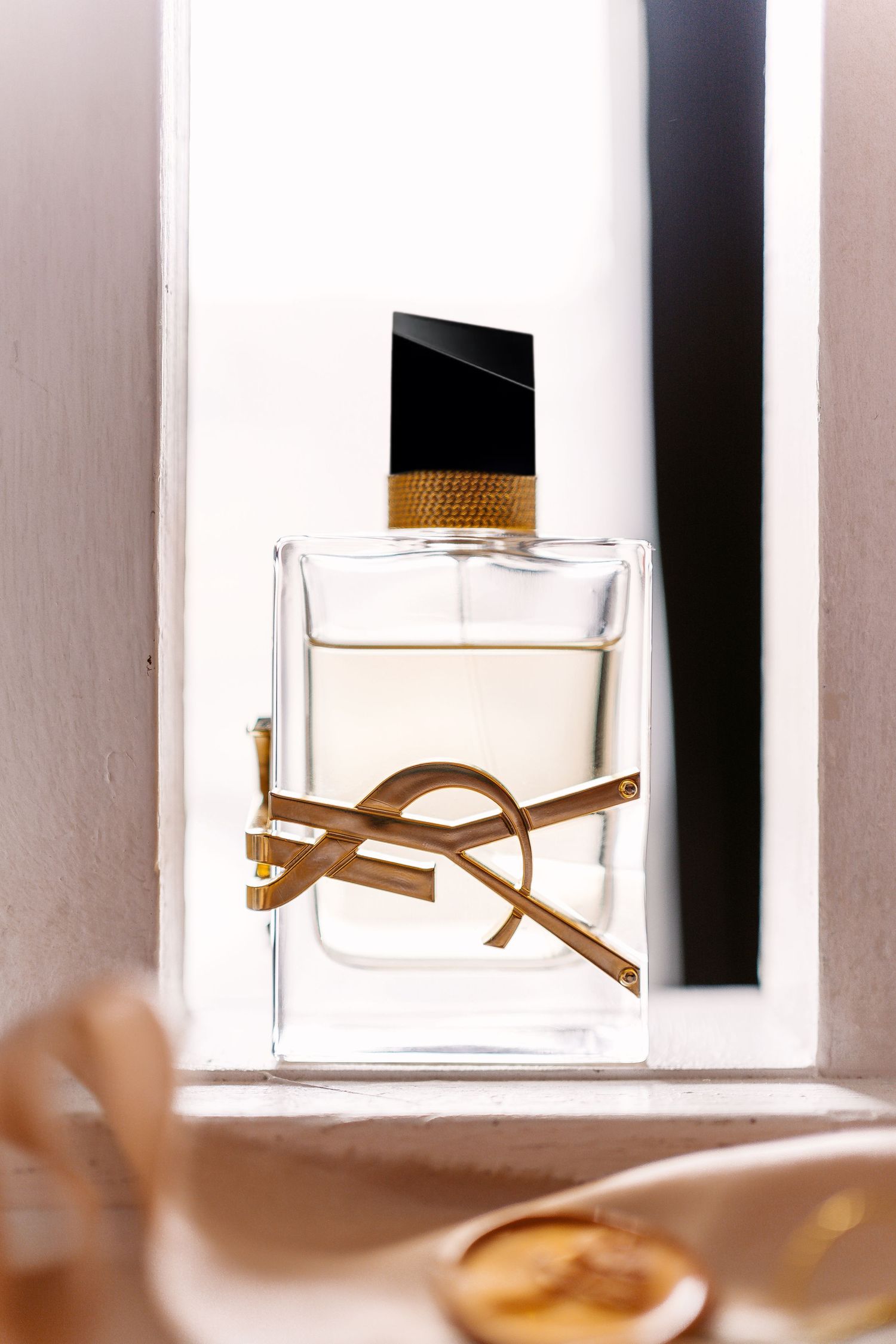 An elegant YSL perfume bottle with golden logo displayed on a white surface in soft lighting.