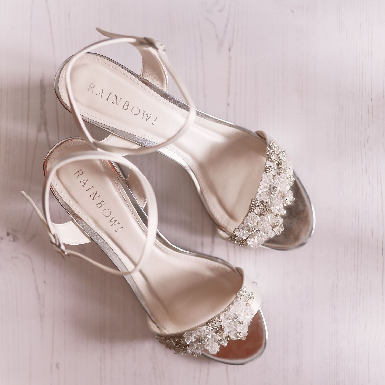 Elegant silver bridal sandals with crystal embellishments on a light wooden surface.