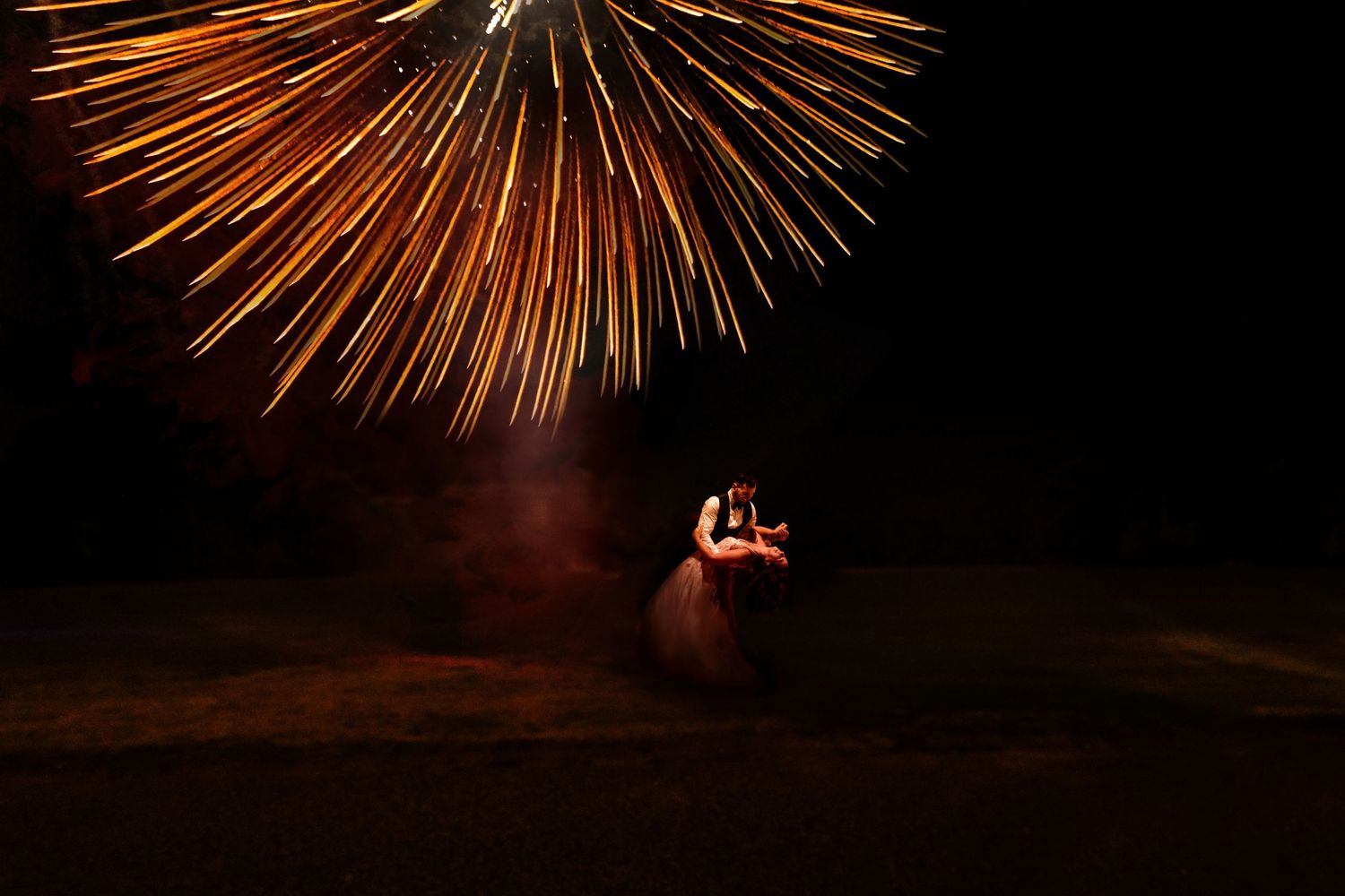 Large orange firework explodes in the night sky during an intimate celebration.