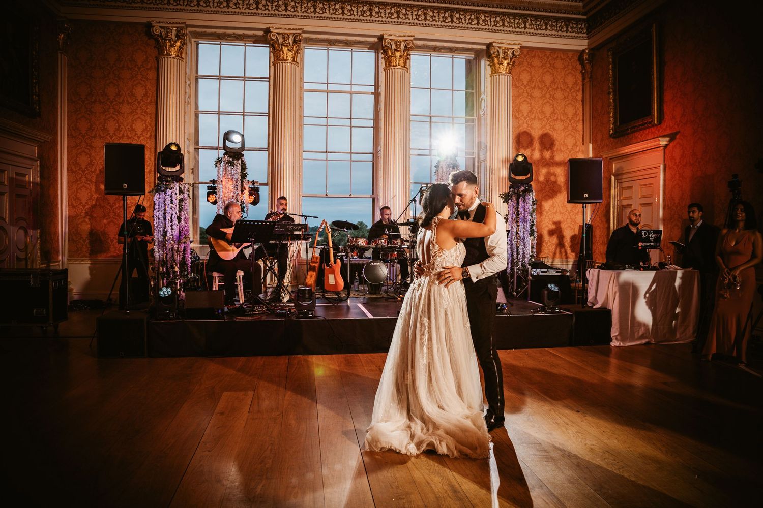 Couple dances in an elegant ballroom with a live band performing on stage in the background.