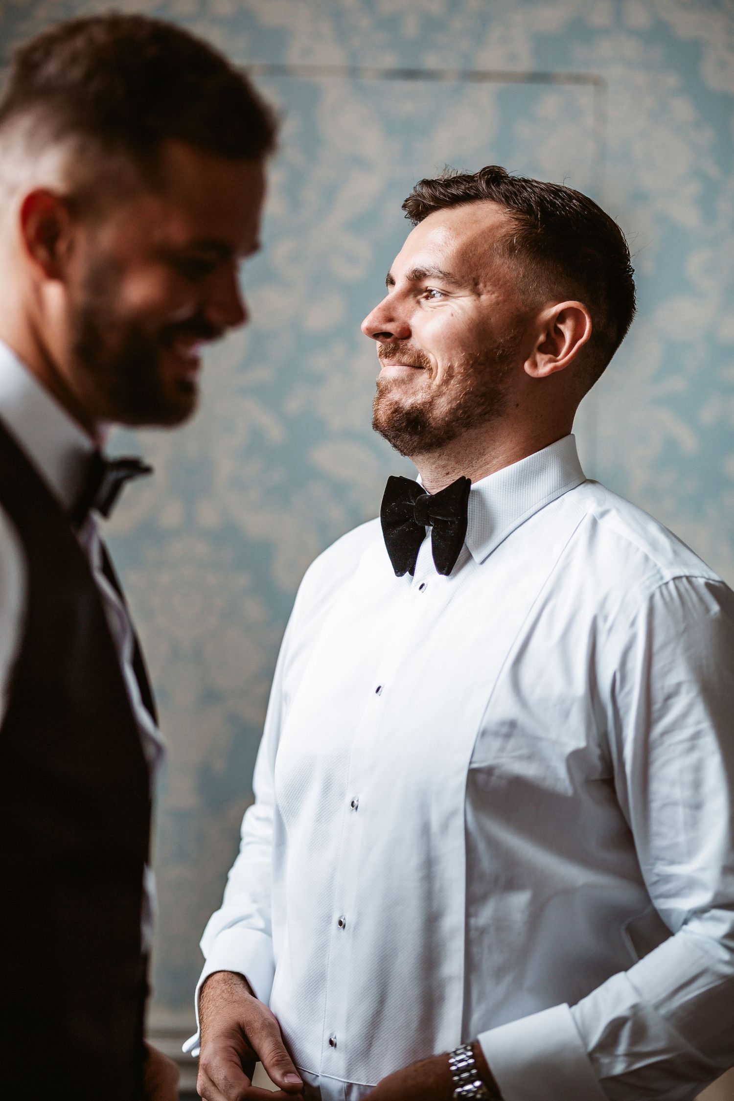 Two people in formal attire sharing a candid moment against a blue damask wallpaper background.