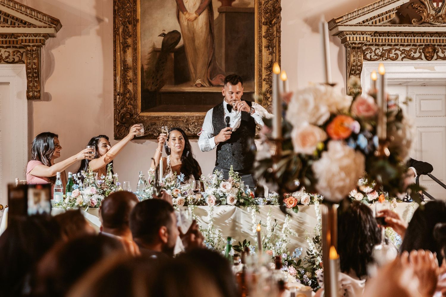 Wedding reception speech in elegant dining room with floral centerpieces and classical decor.