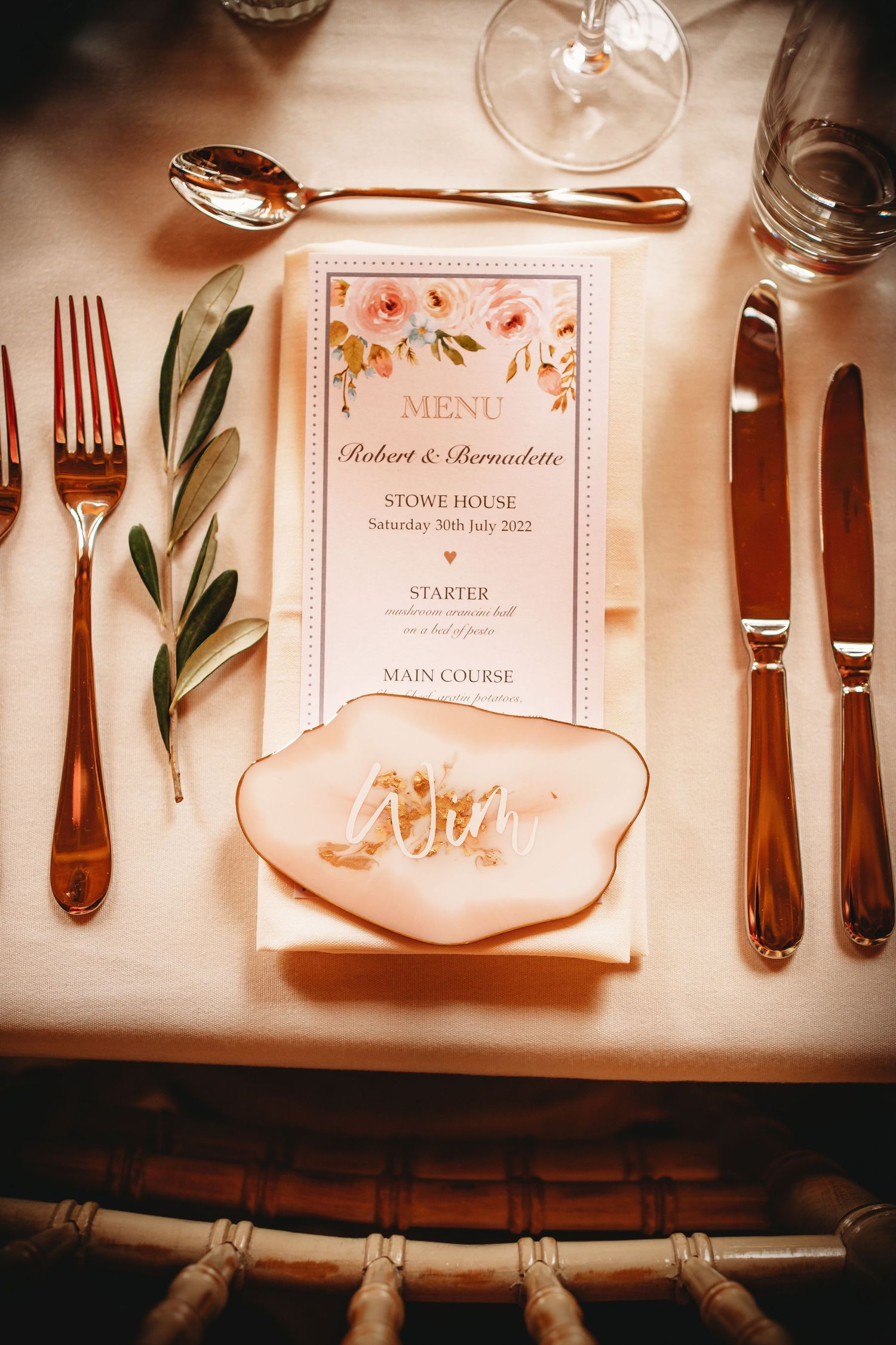 Elegant place setting with menu card, gold flatware, and pink agate name card holder.