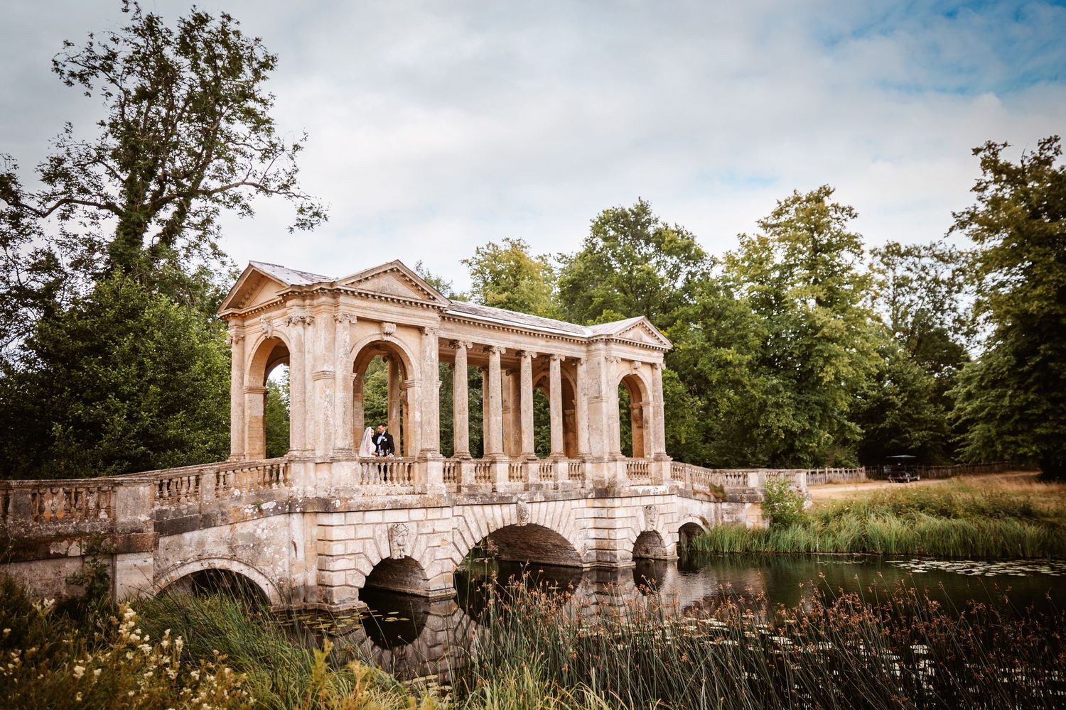 Historic stone bridge and archway structure in formal garden setting.