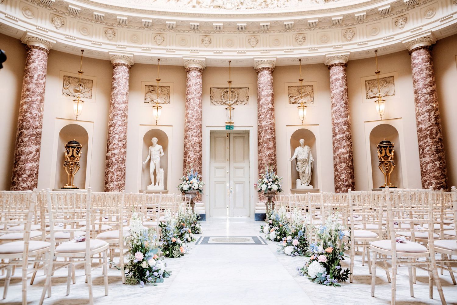 Elegant wedding ceremony venue with marble columns and statues in classical round room setting.