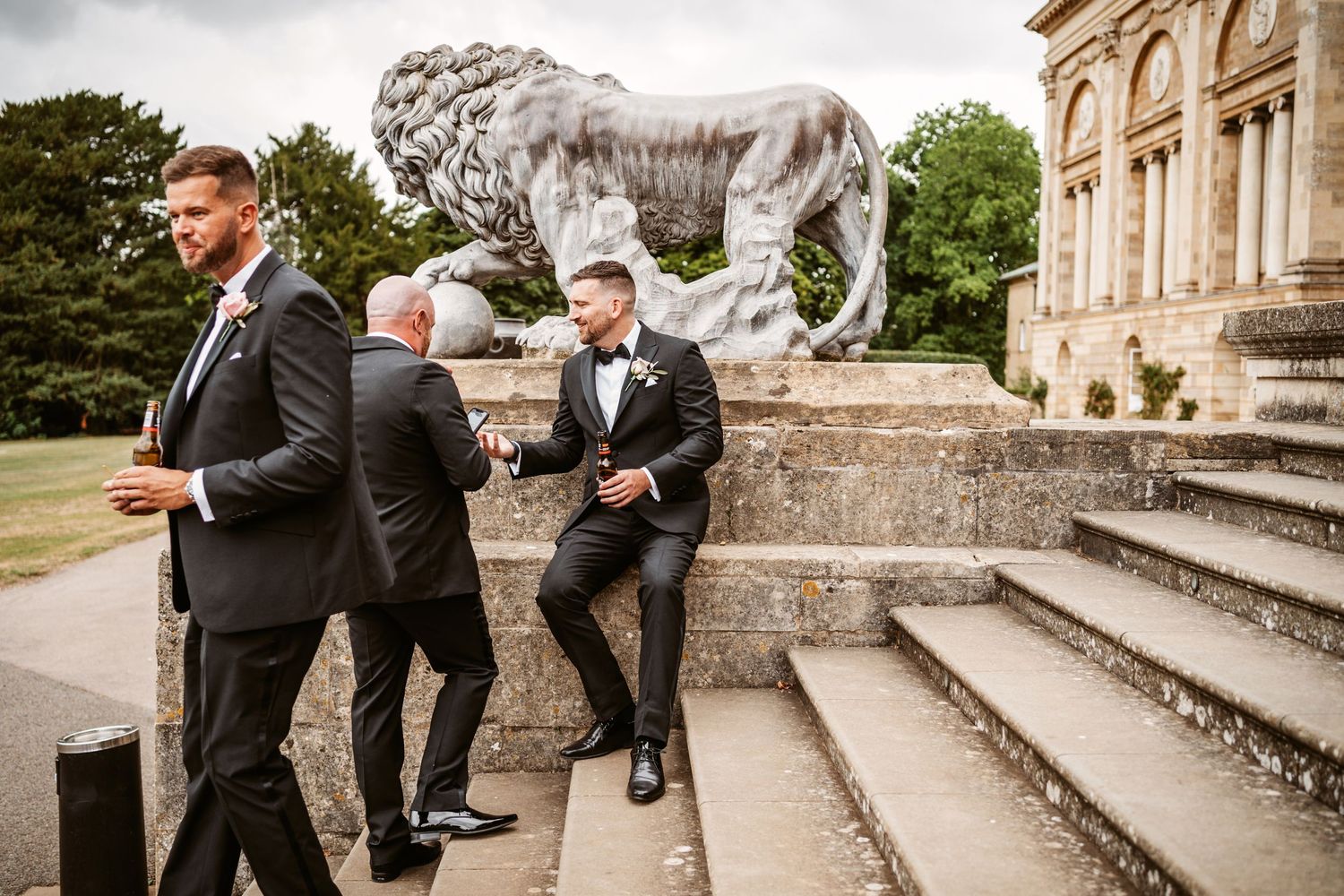 Groomsmen posing near stone lion statue outside historic building.
